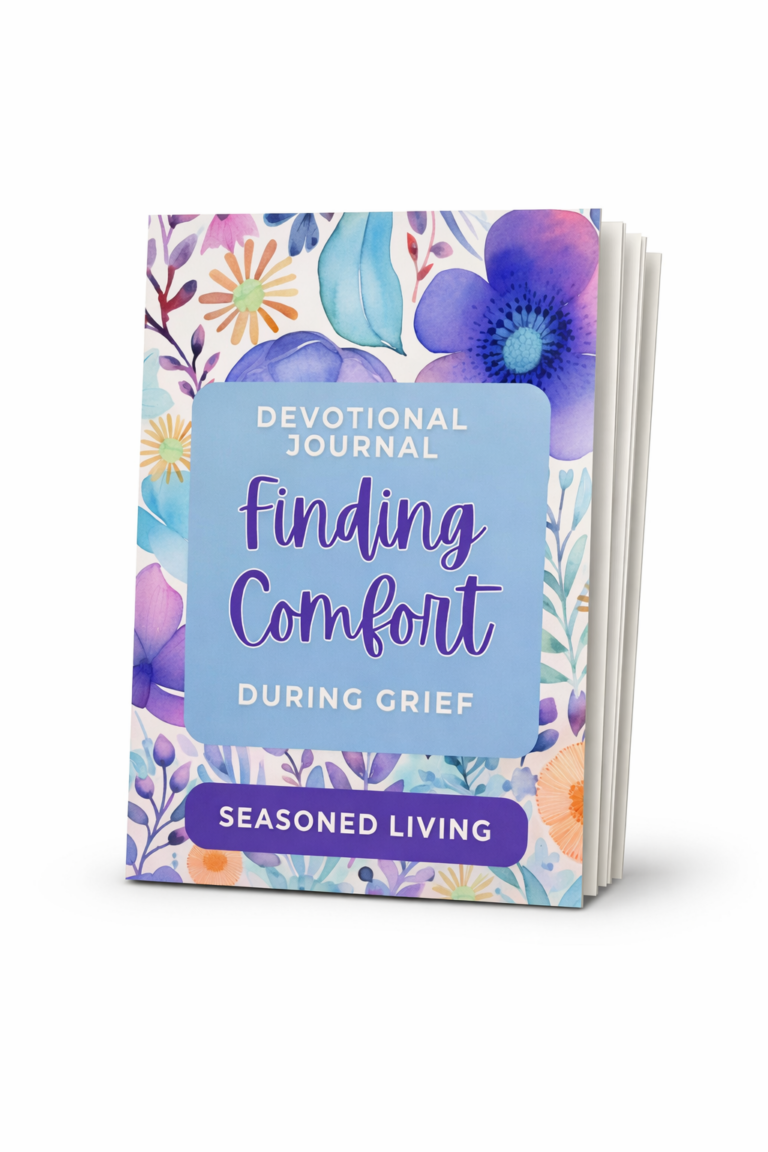 Professional mock‑up of the devotional journal “Finding Comfort During Grief” by Seasoned Living, standing upright with fanned‑out pages and watercolor floral cover in shades of blue, purple, and orange.